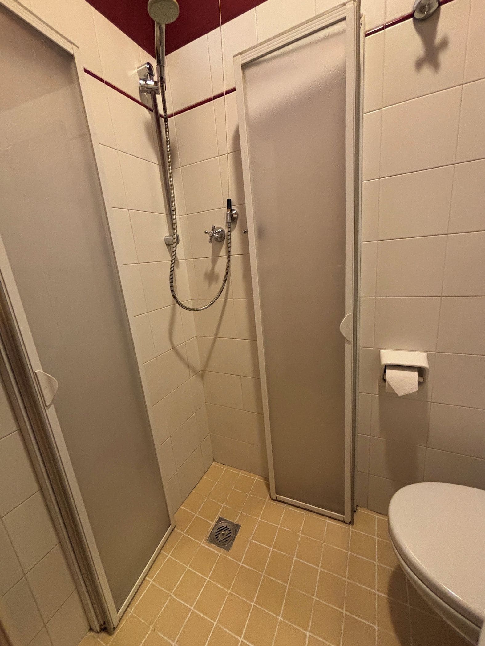 A small, enclosed shower stall with a door, a toilet, and a towel dispenser.