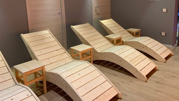 Um espaço com espreguiçadeiras de madeira e pequenas mesas, provavelmente uma área de spa ou relaxamento.
