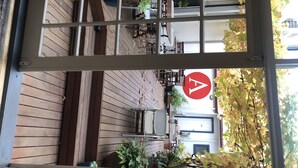 A view through a window of a wooden deck area with outdoor furniture and plants.