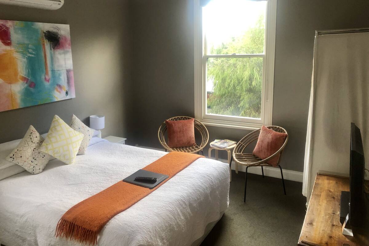 A bedroom with a bed, two wicker chairs, a small table, and a window with a view of trees.