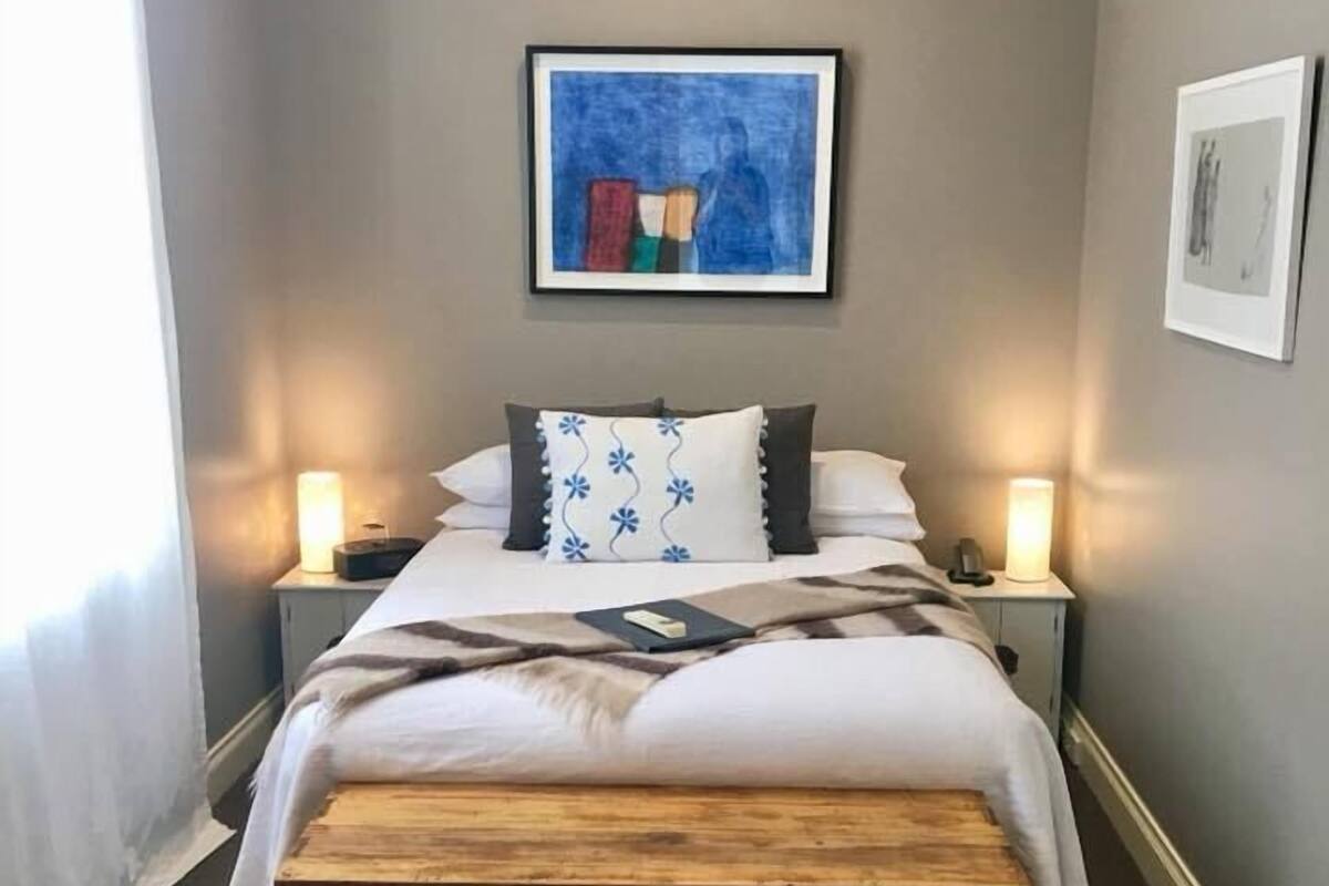 A bedroom with a bed, bedside tables, a nightstand, a wooden bench, and artwork on the walls.