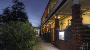 A building with a brick facade, a balcony, and a pathway leading to the entrance.