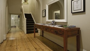 A hallway with wooden flooring, a staircase, a desk with papers, and framed certificates on the wall.