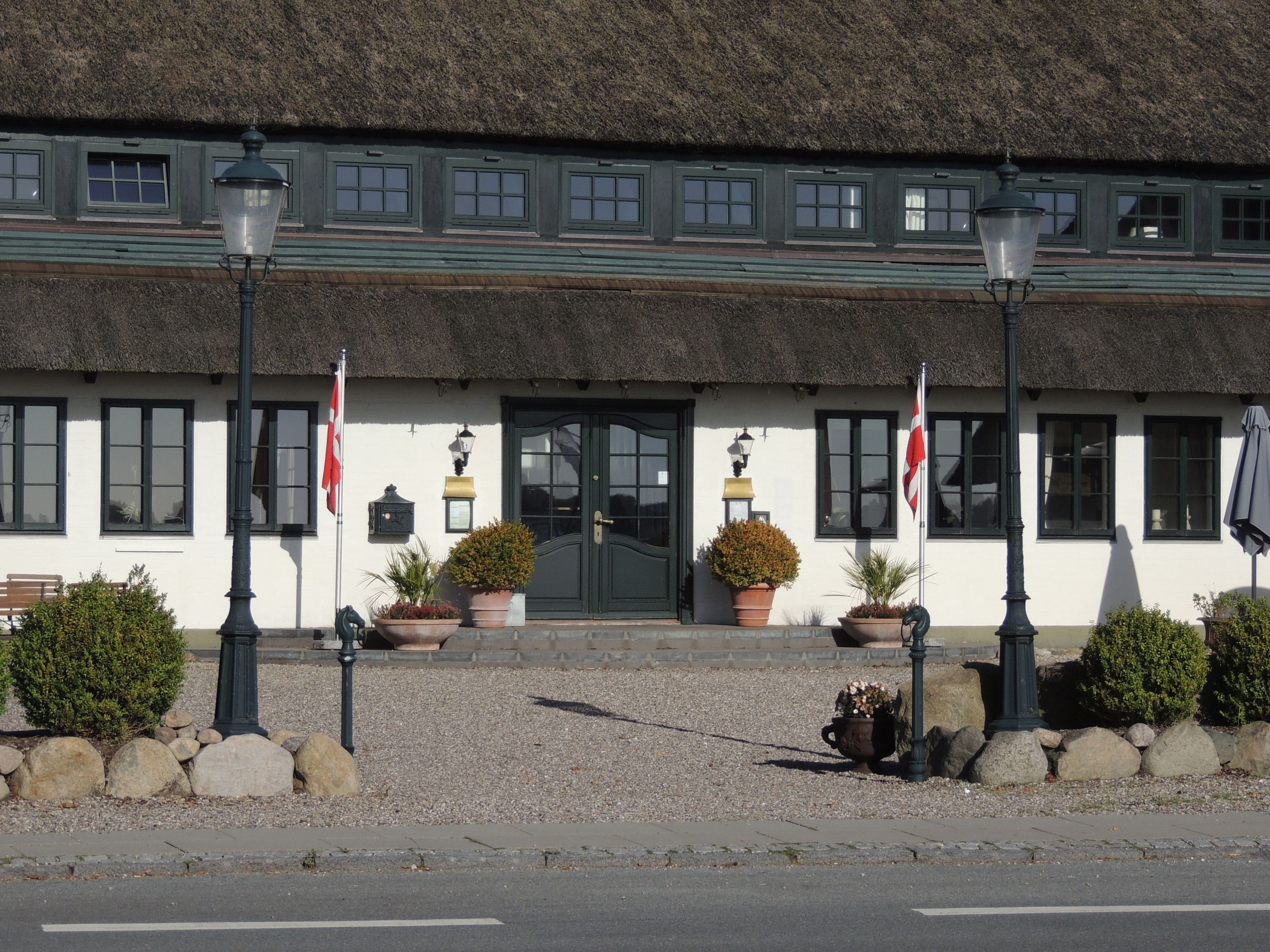A building with a thatched roof, multiple windows, and a door. There are potted plants and a bench outside.