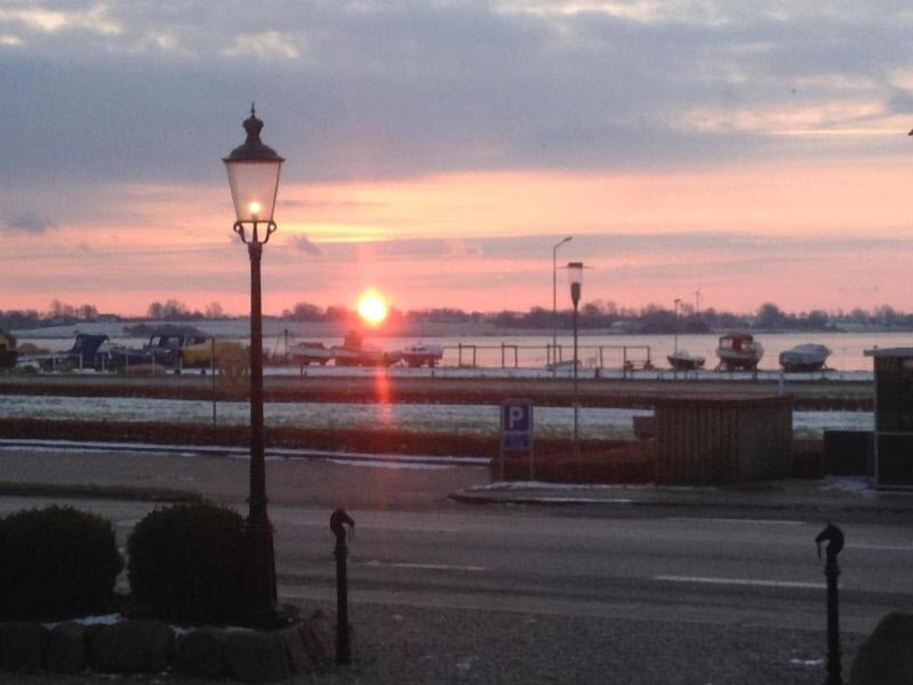 A sunset over a body of water with a parking sign and a lamp post in the foreground.