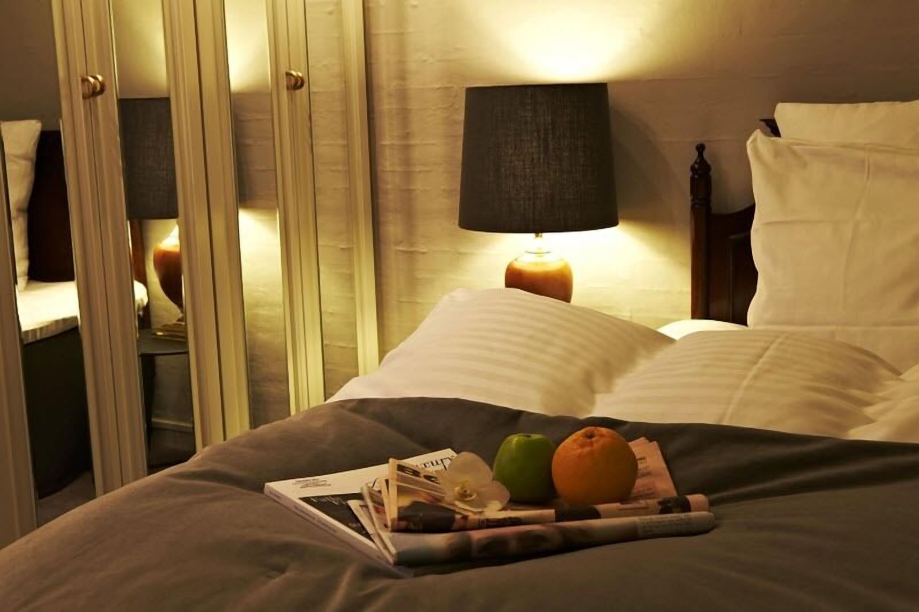 A hotel room with a bed, a nightstand with a lamp, and a mirror.