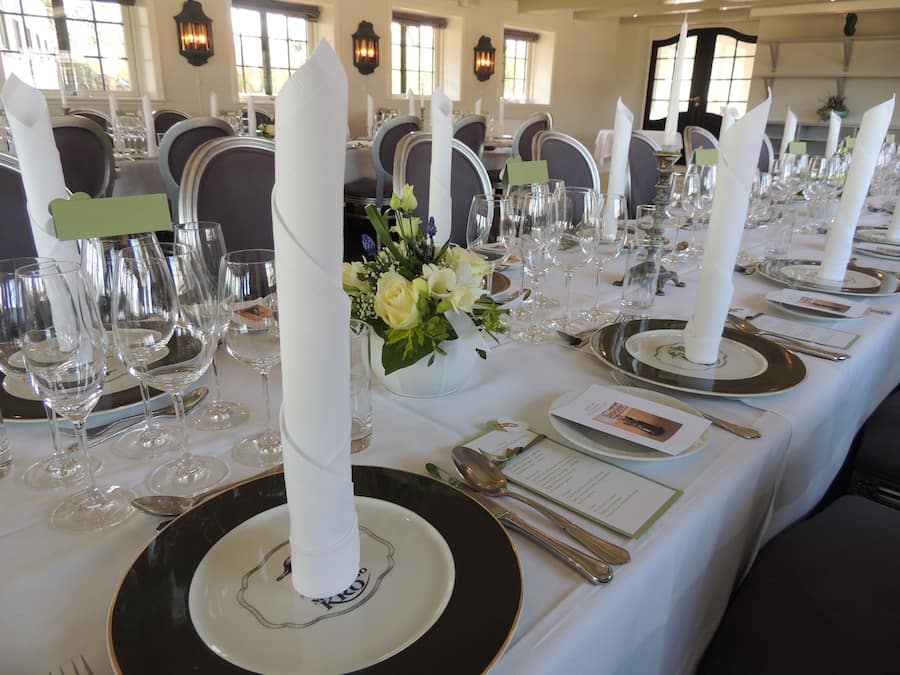 Une table à manger élégante, dressée avec des serviettes blanches, des assiettes noires et de la verrerie transparente.