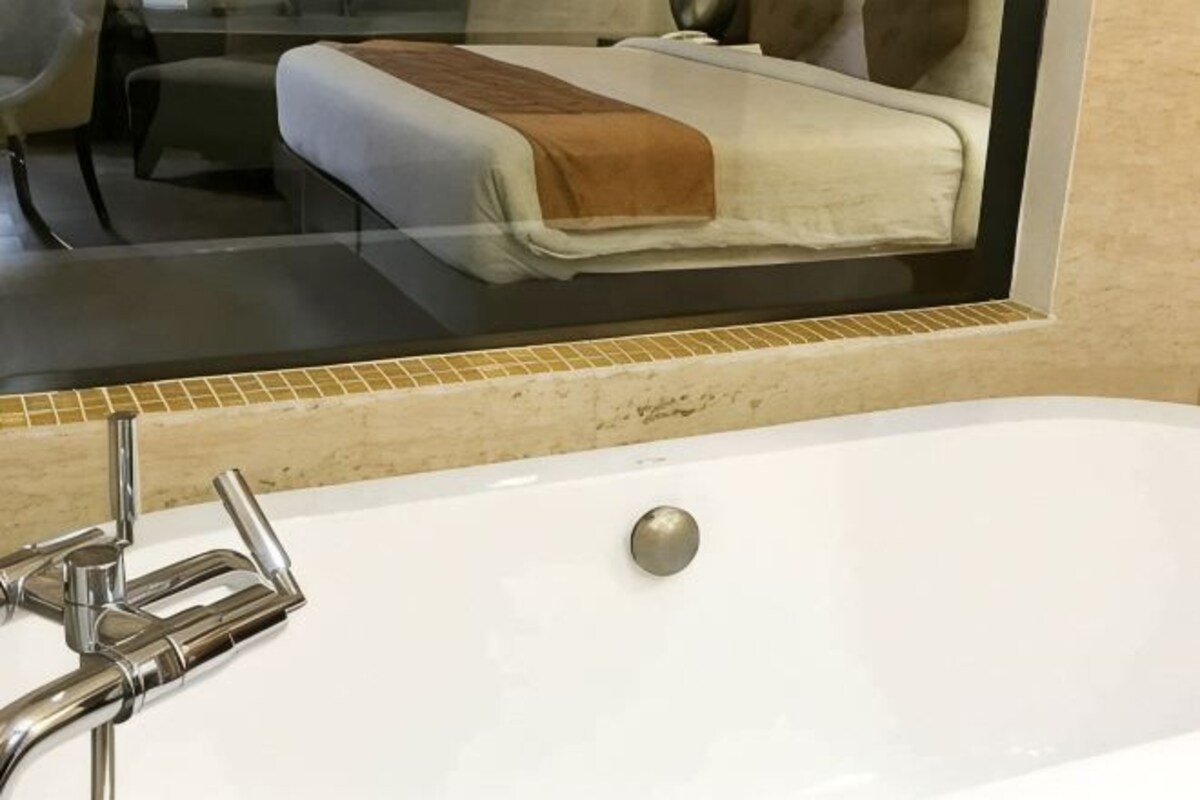 A bathroom with a white bathtub, a mirror, and a bed with a brown blanket.