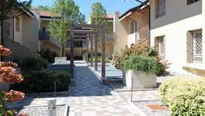 En gård med et skakternet flisegang, en pergola og plantekasser.