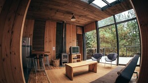 A cozy cabin interior with a wooden interior, a large window overlooking a forest, a wooden bench, and a television.