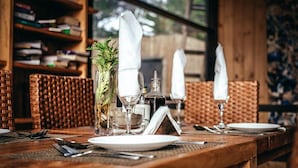 A dining table set with white plates, cutlery, and glassware, with a vase of greenery and a menu stand.