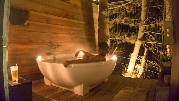 A wooden cabin with a large bathtub and a glass of drink on a wooden table.