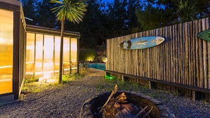 A wooden fence with a surfboard decoration, a fire pit, and a pool area with chairs and a table.