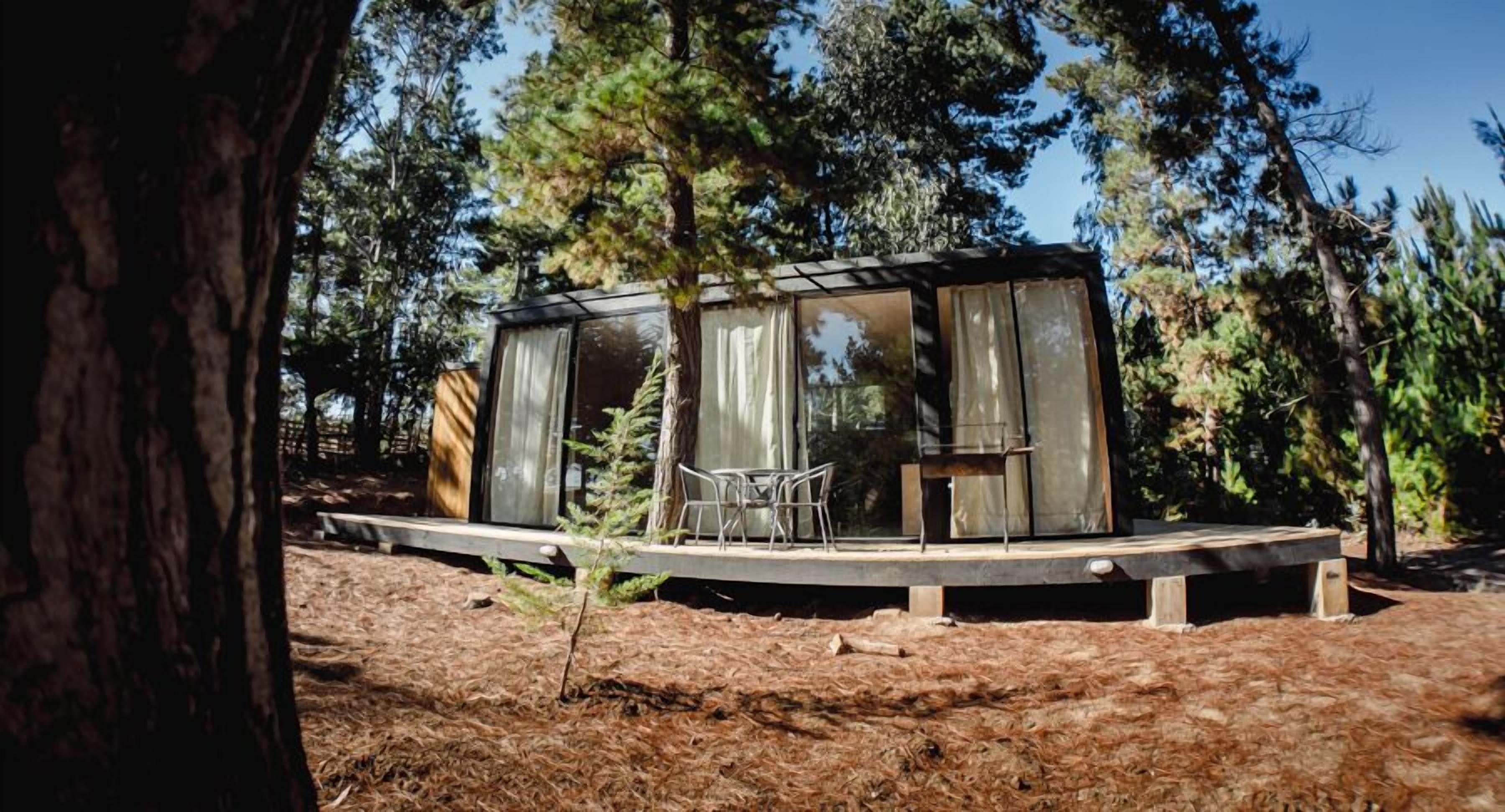 A cabin with a glass enclosure, wooden deck, and a dining area with chairs.