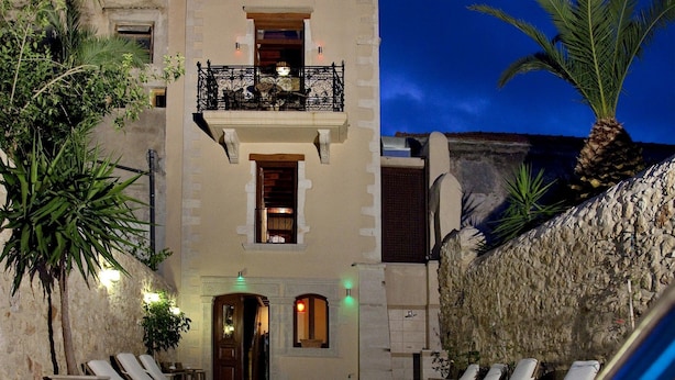 A pool area with lounge chairs, a stone wall, and a building with balconies. - Antica Dimora Suites (Rethymno)