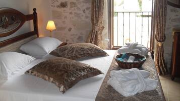 A bed with two pillows, a bedside lamp, a basket with towels, and a window with curtains.