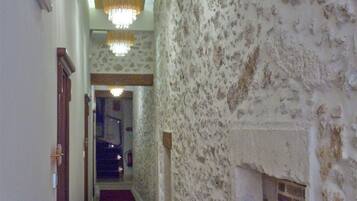 A hallway with a red carpet, stone walls, a brick fireplace, and a chandelier.