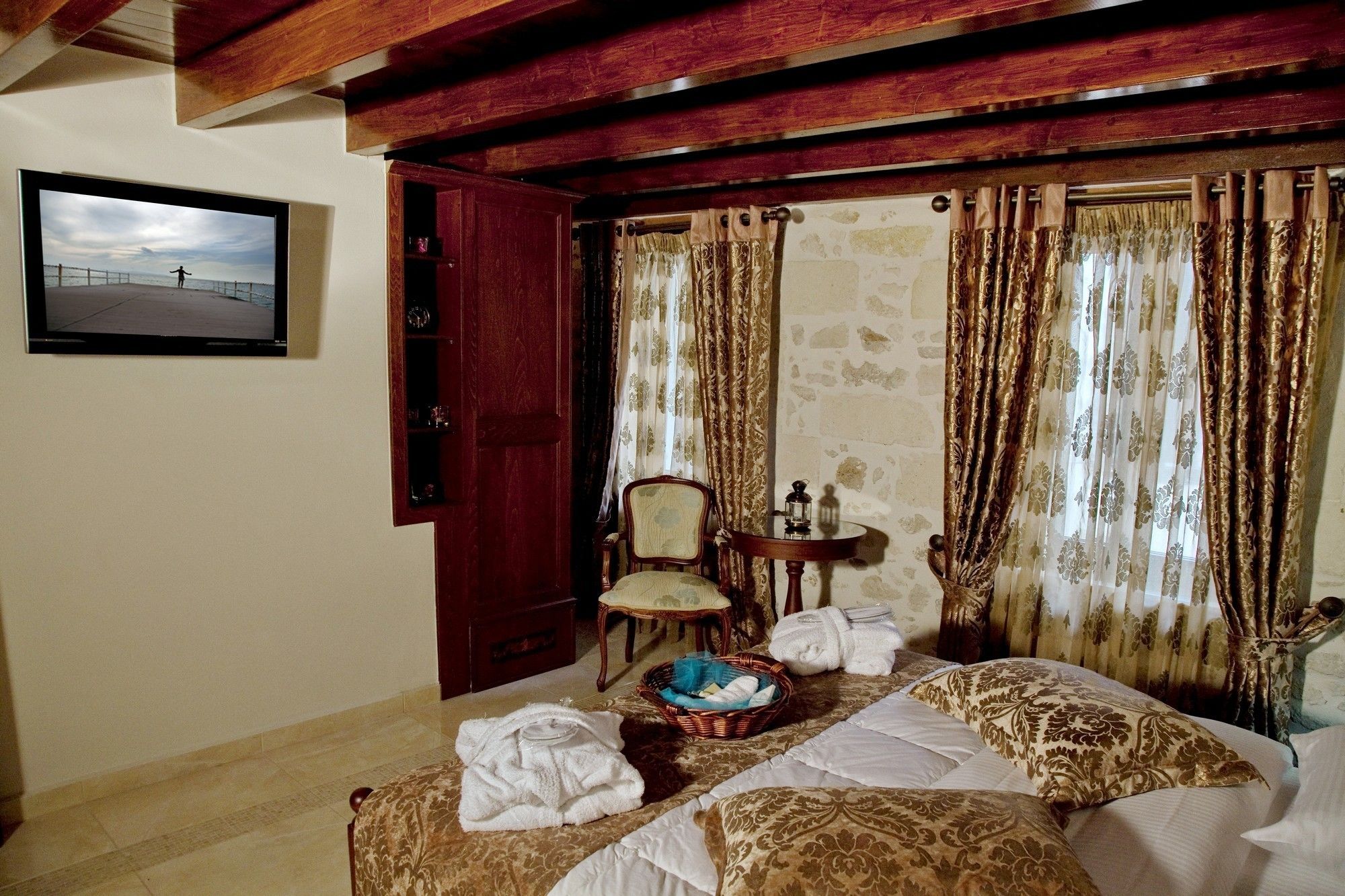 A room with a bed, a chair, a table with a lantern, and a wall-mounted TV.