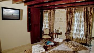 A room with a bed, a chair, a table with a lantern, and a wall-mounted TV.