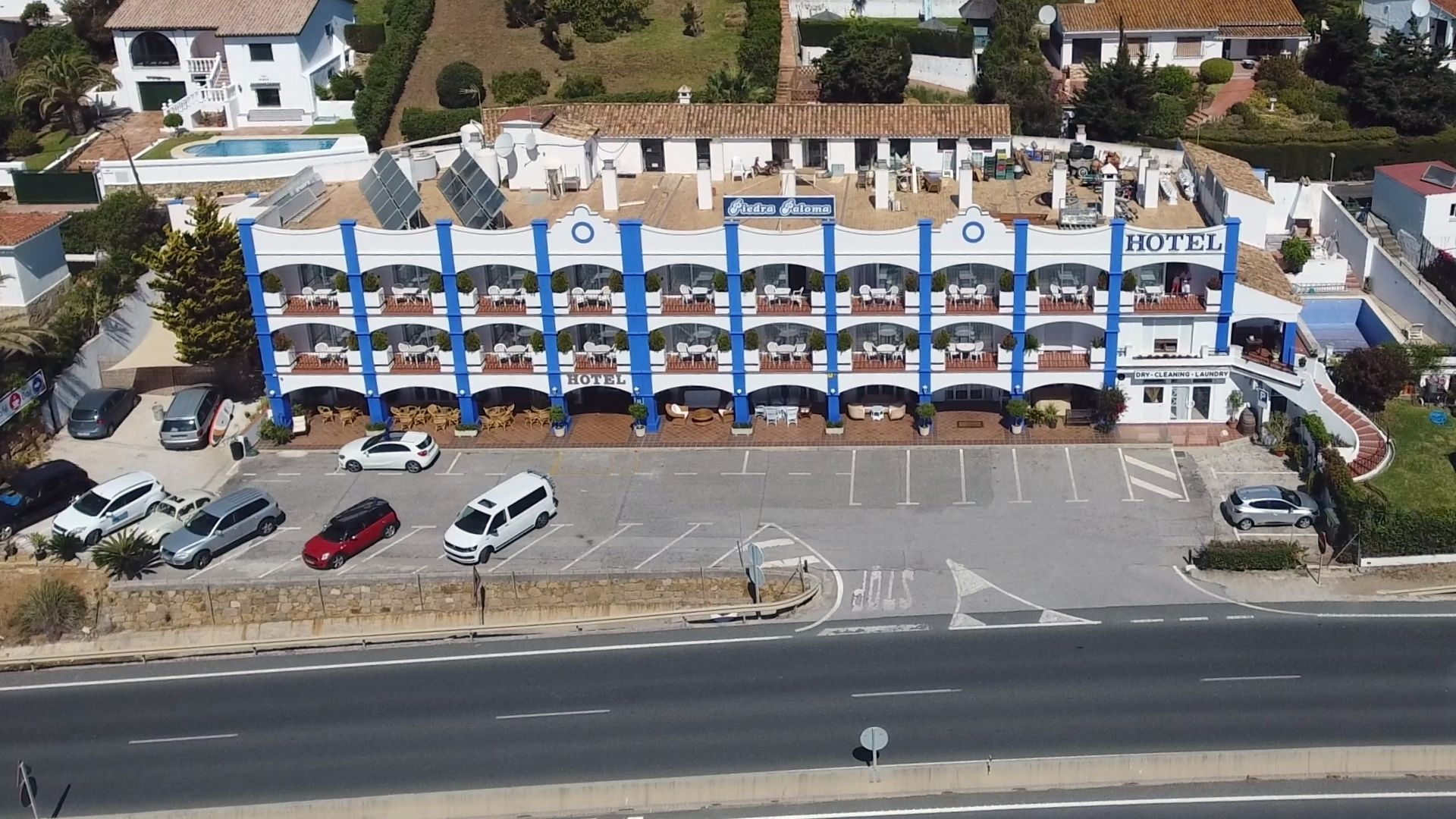 Eine Vogelperspektive eines Hotels mit mehreren Balkonen, einem Schwimmbad und einem Parkplatz.