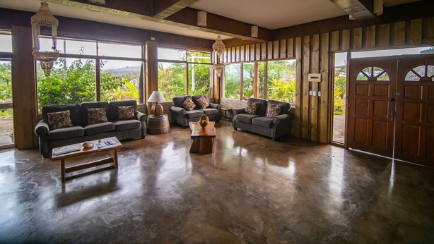 A spacious living room with large windows, a wooden ceiling, and a view of greenery outside. - Tupa Hotel (Hanga Roa)
