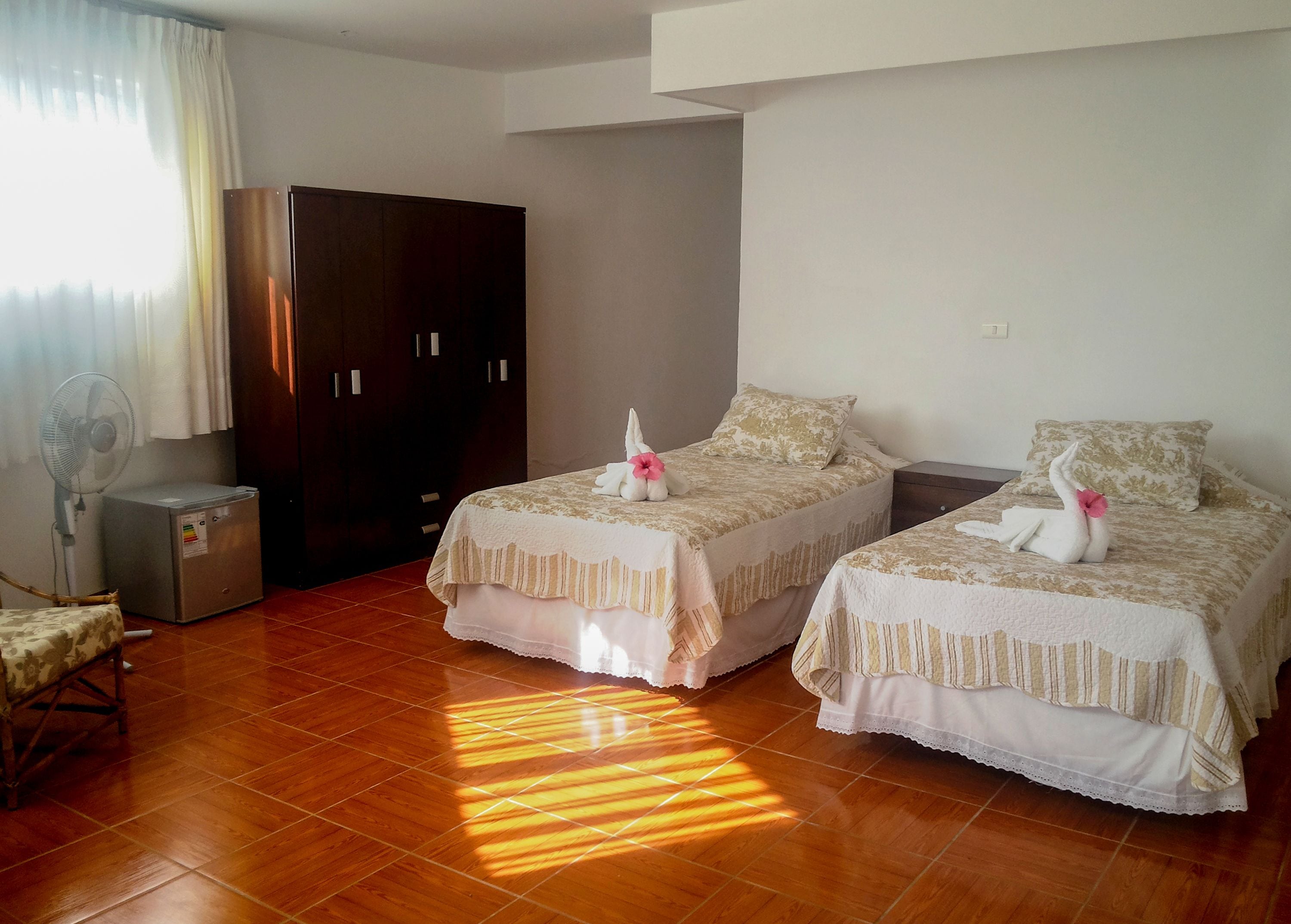 A hotel room with two beds, a wardrobe, a desk, and a fan.