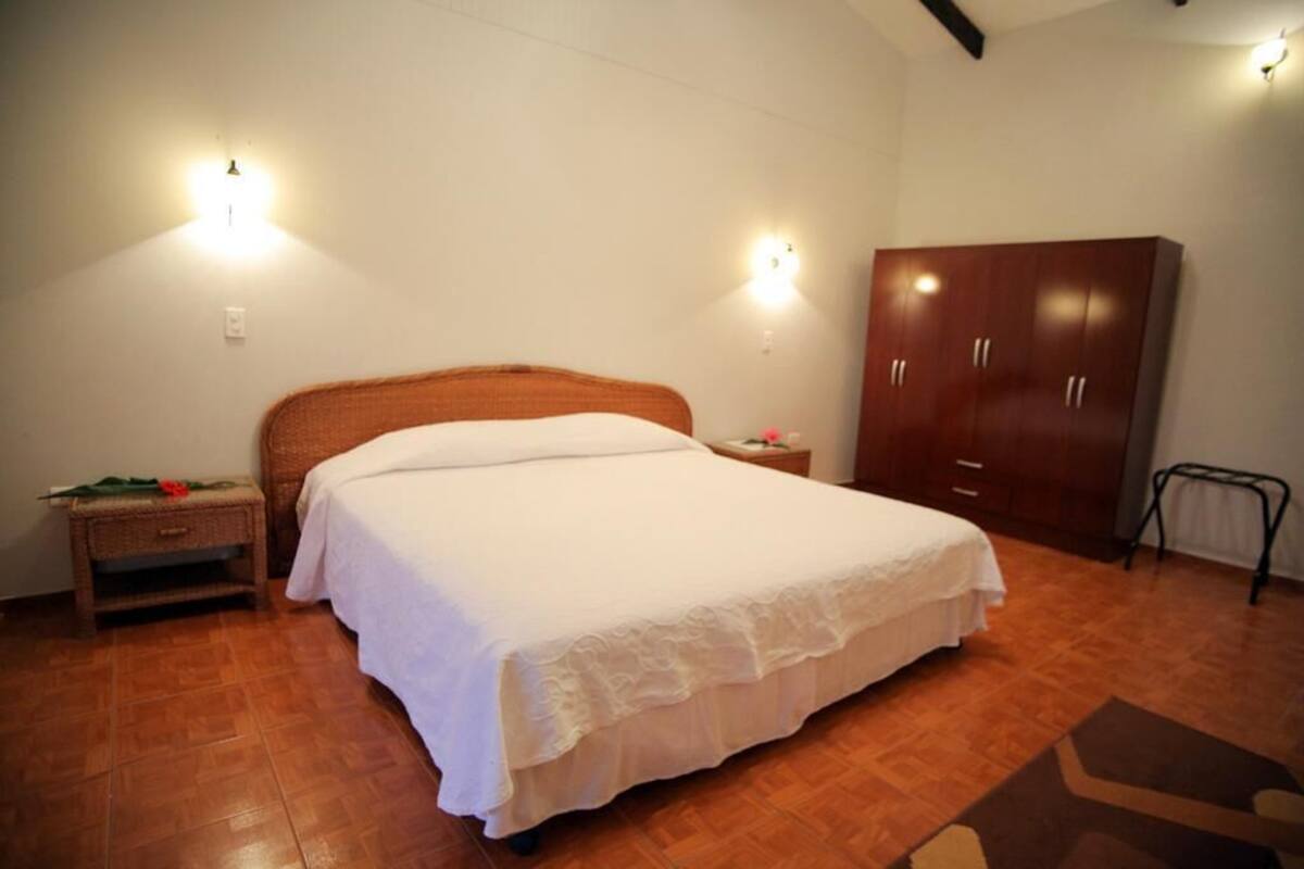 A bedroom with a bed, wooden wardrobe, nightstand, and wall-mounted lights.