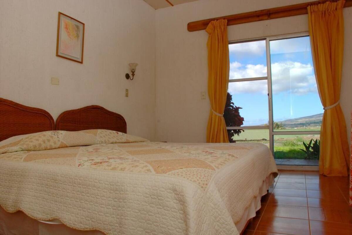 A bedroom with a bed, a window with curtains, a wall-mounted light, and a framed picture.