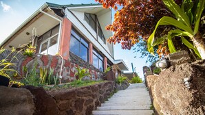 A staircase leading to a house with a stone wall on one side and a garden with plants and a mural on the other. - Tupa Hotel (Hanga Roa)