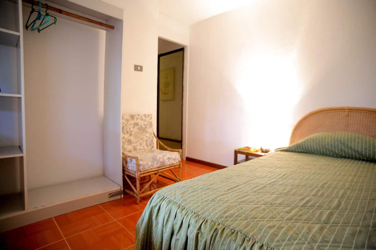A bedroom with a bed, a chair, a wardrobe, and a small table.