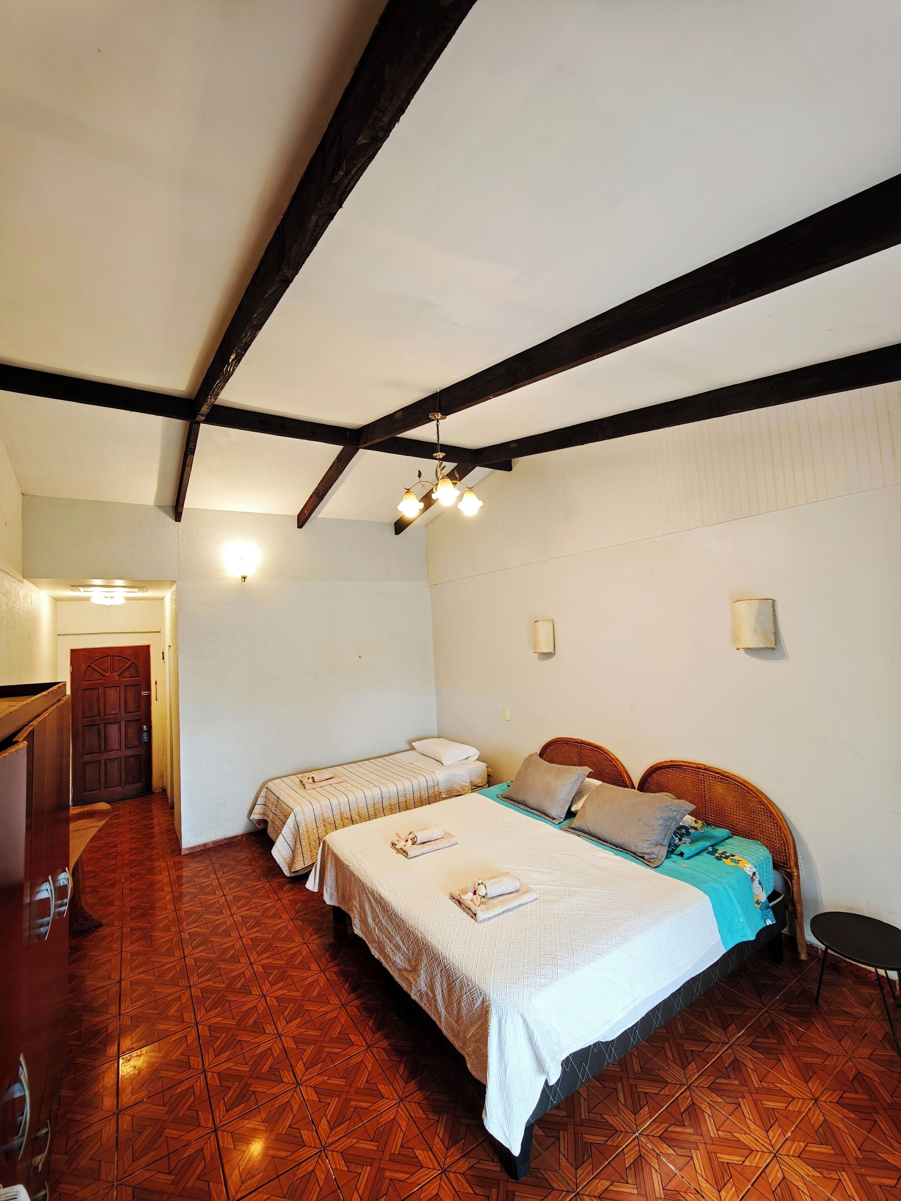 A room with two single beds, a wooden floor, a wooden ceiling beam, and a door.