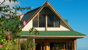 A two-story house with a green roof, large windows, and a view of the ocean. - Tupa Hotel (Hanga Roa)