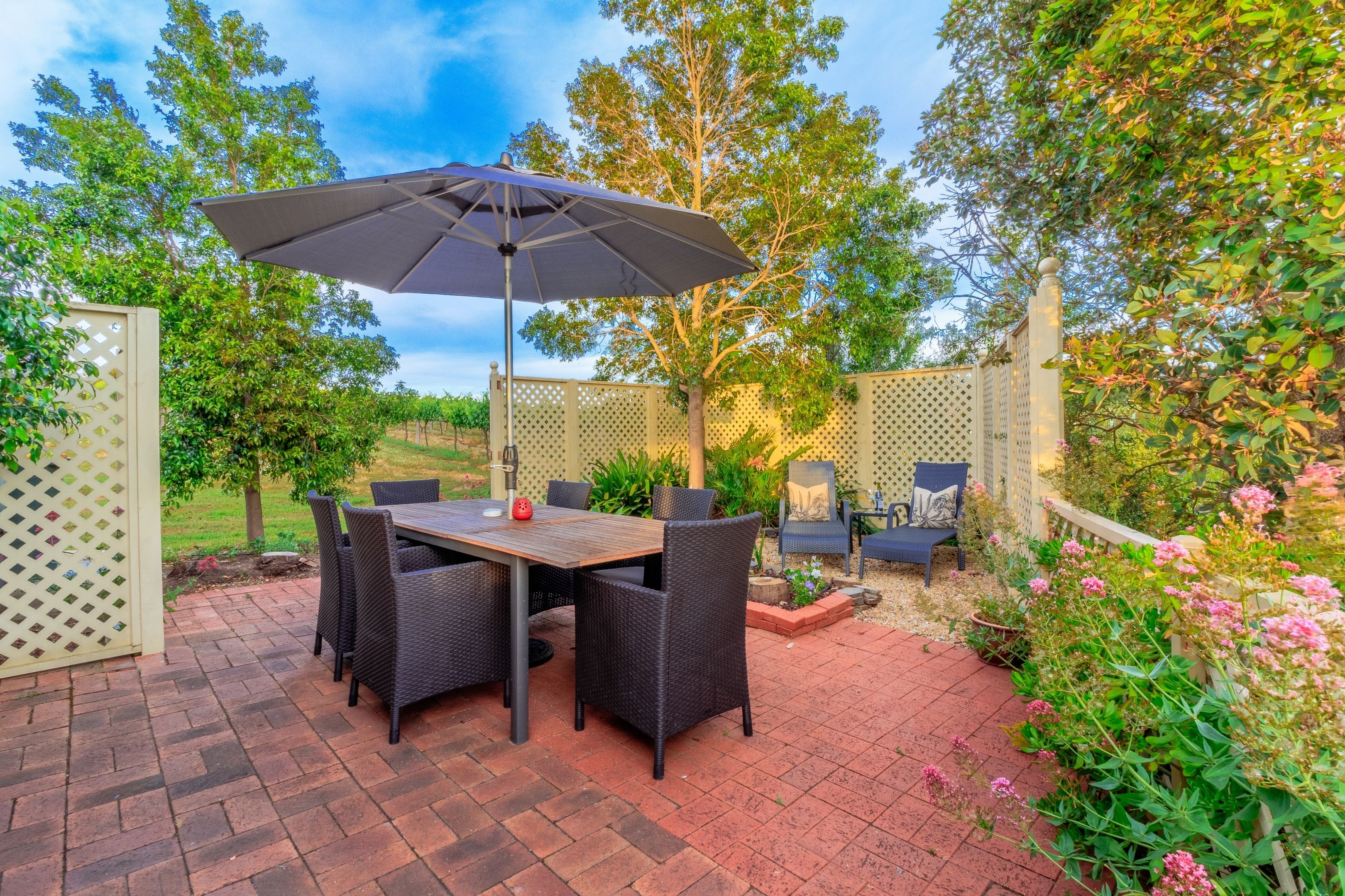 An outdoor patio with a table and chairs, surrounded by a fence and greenery.