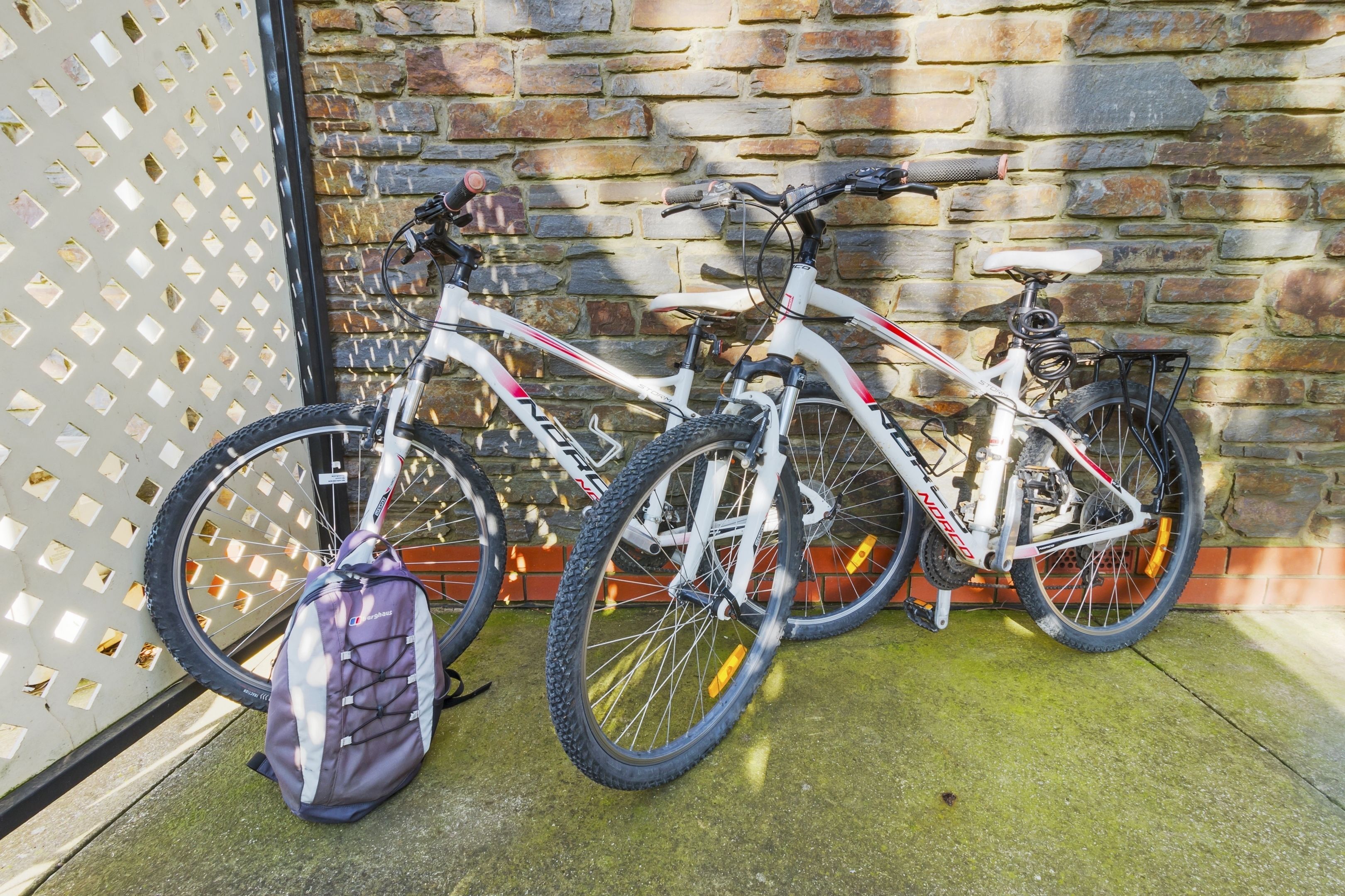 Dos bicicletas estacionadas frente a un muro de ladrillo con una valla enrejada al fondo.