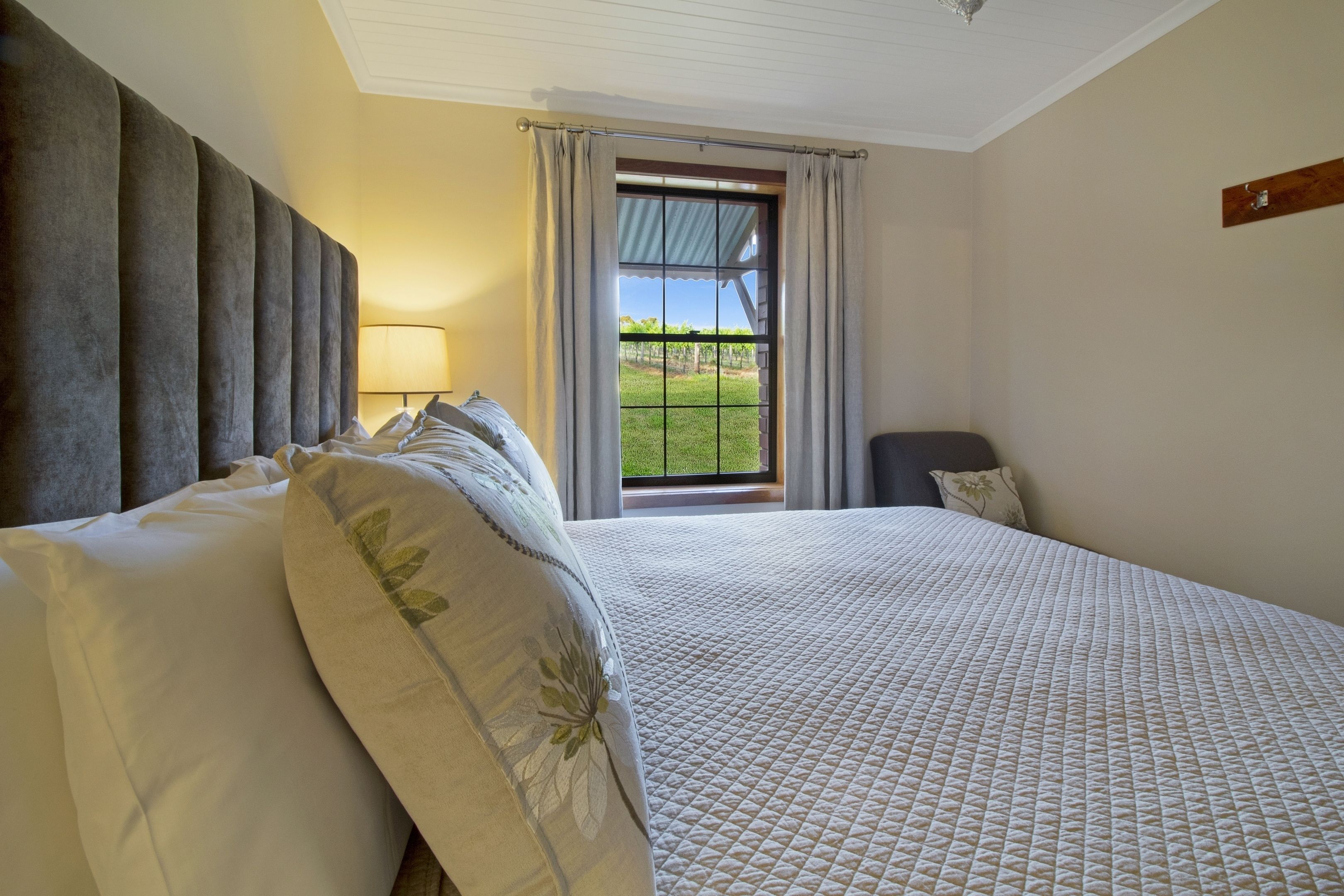 Una camera da letto con un letto grande, una finestra vista su un paesaggio verde e una testiera con pannelli verticali.