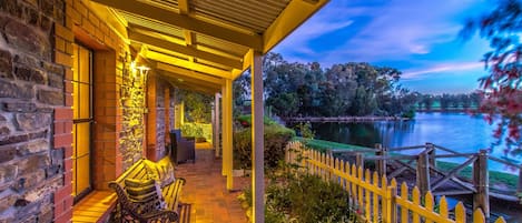 A covered patio with a brick wall, a bench, and a view of a lake at dusk.