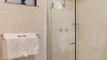 Une douche fermée par des parois en verre, dotée d’un pommeau de douche à main, d’un porte-serviettes avec des serviettes blanches et d’un buste décoratif accroché au mur.