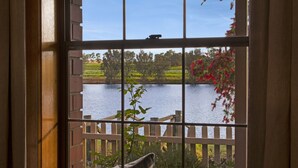 A view through a window with a wooden bench and a fence overlooking a body of water and greenery.