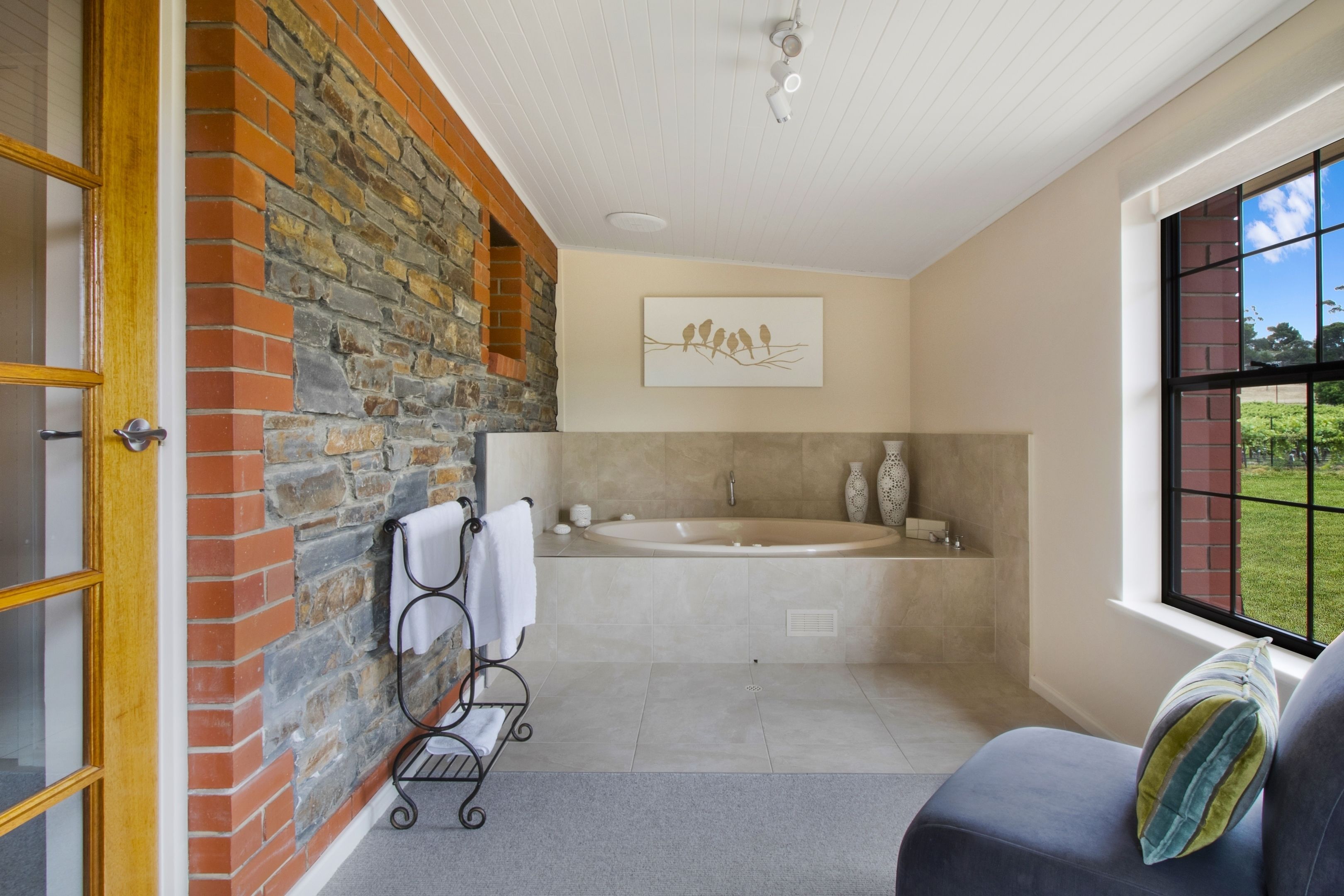 A bathroom with a stone wall, a bathtub, a towel rack, and a window with a view.