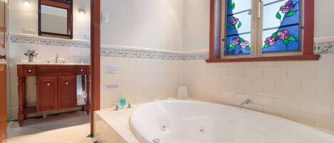 Un baño con una bañera grande, un tocador de madera y una ventana con vitrales.