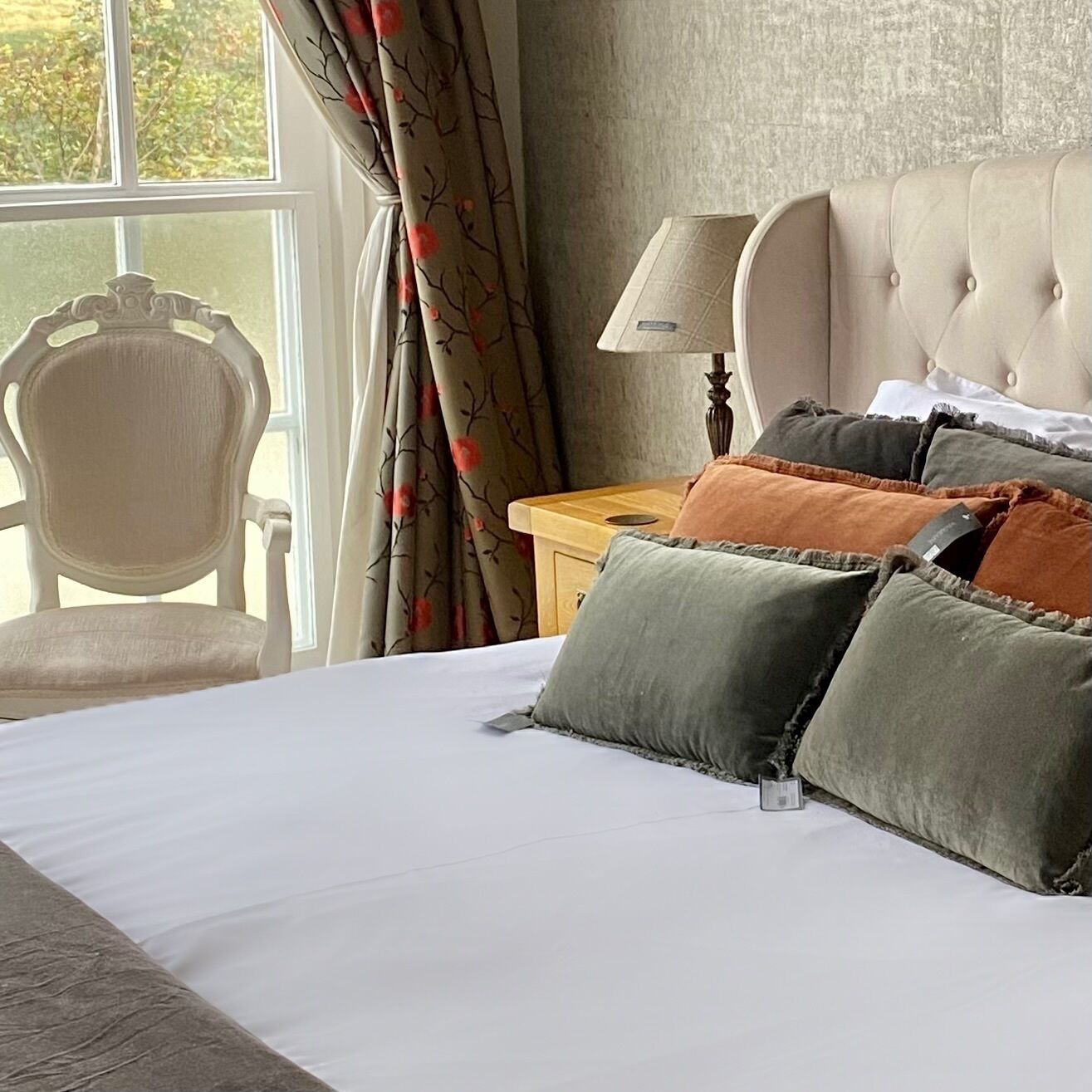 A hotel room with a bed, a chair, a nightstand, a lamp, and a window with curtains.