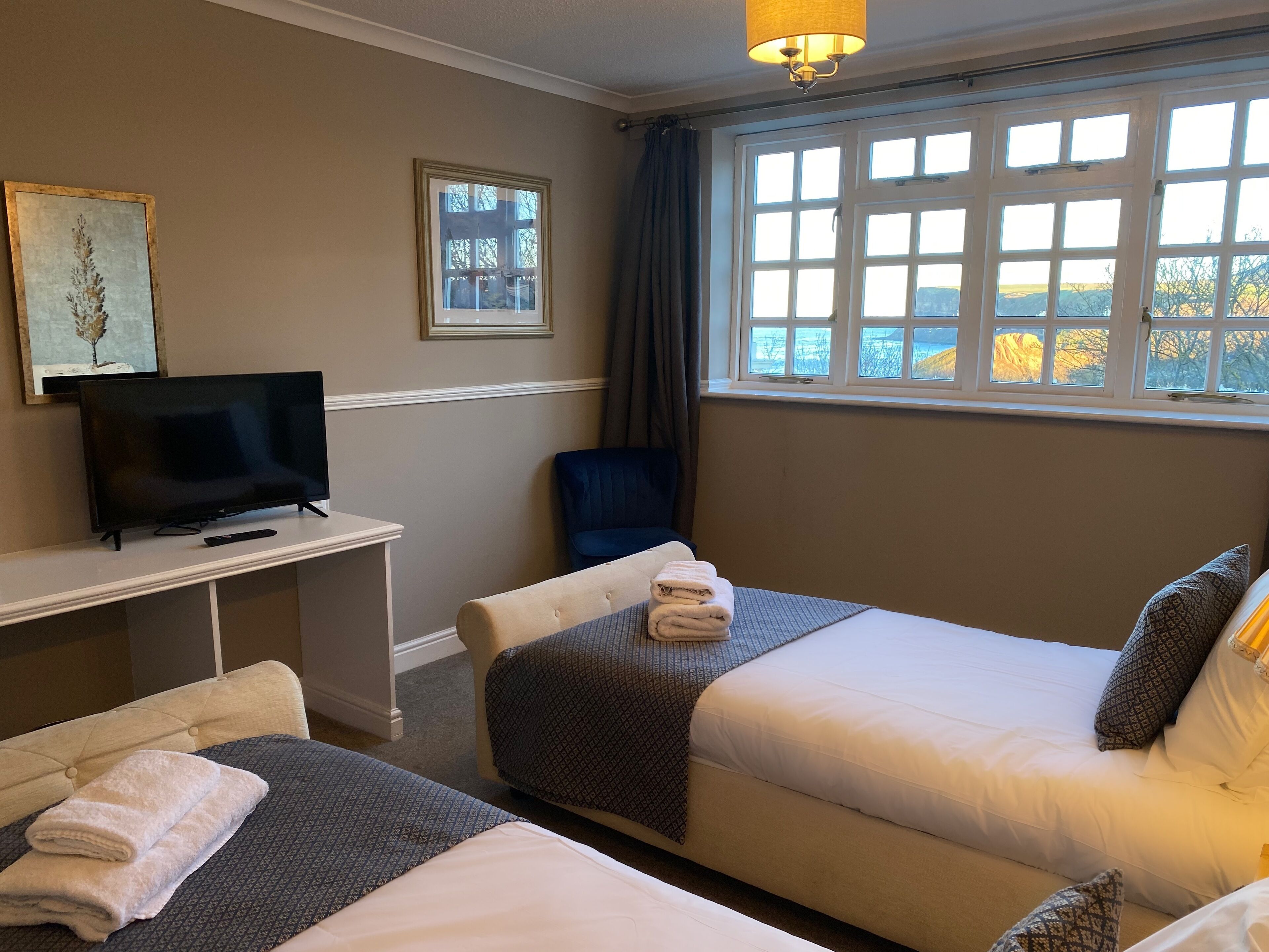 A hotel room with two beds, a TV, a desk, and a window with a view.