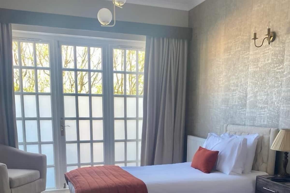A hotel room with two beds, a chair, a lamp, and a view through a large window.