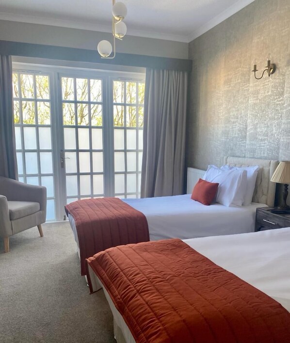A hotel room with two beds, a chair, a lamp, and a view through a large window. - The Spa Hotel (Saltburn-by-the-Sea)
