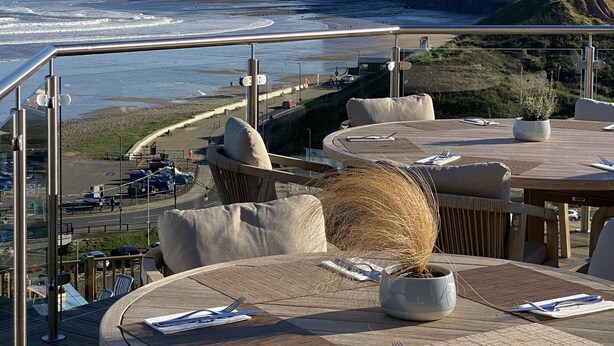 A seaside terrace with round tables and wicker chairs, overlooking a beach and cliffs. - The Spa Hotel (Saltburn-by-the-Sea)