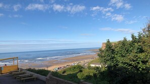 A beach view with a wooden deck and picnic tables, overlooking the ocean and a cliff. - The Spa Hotel (Saltburn-by-the-Sea)