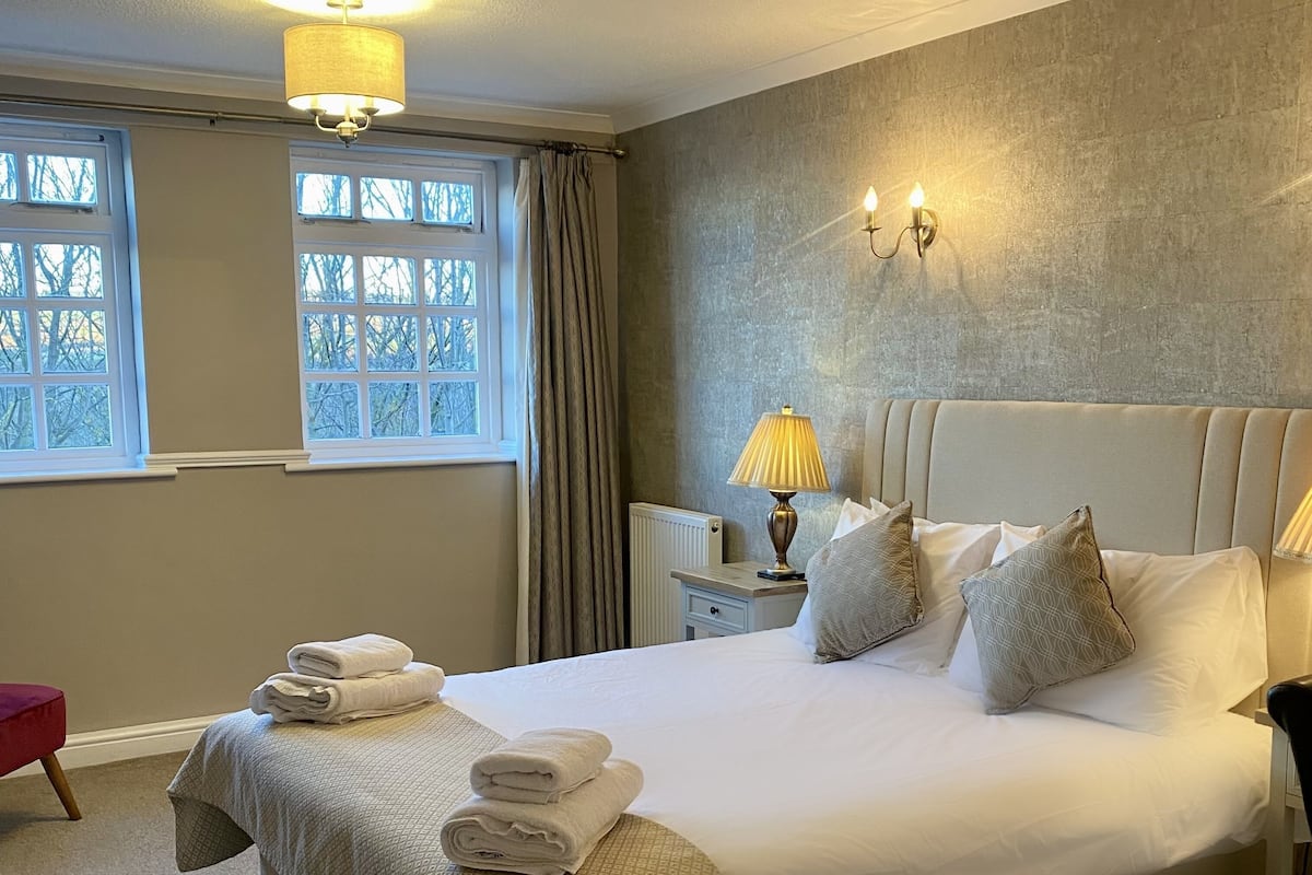A neatly made bed with a headboard, a bedside table with a lamp, and a window with curtains.