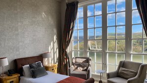 A hotel room with a bed, a chair, a small table, and a view of the countryside through large windows. - The Spa Hotel (Saltburn-by-the-Sea)
