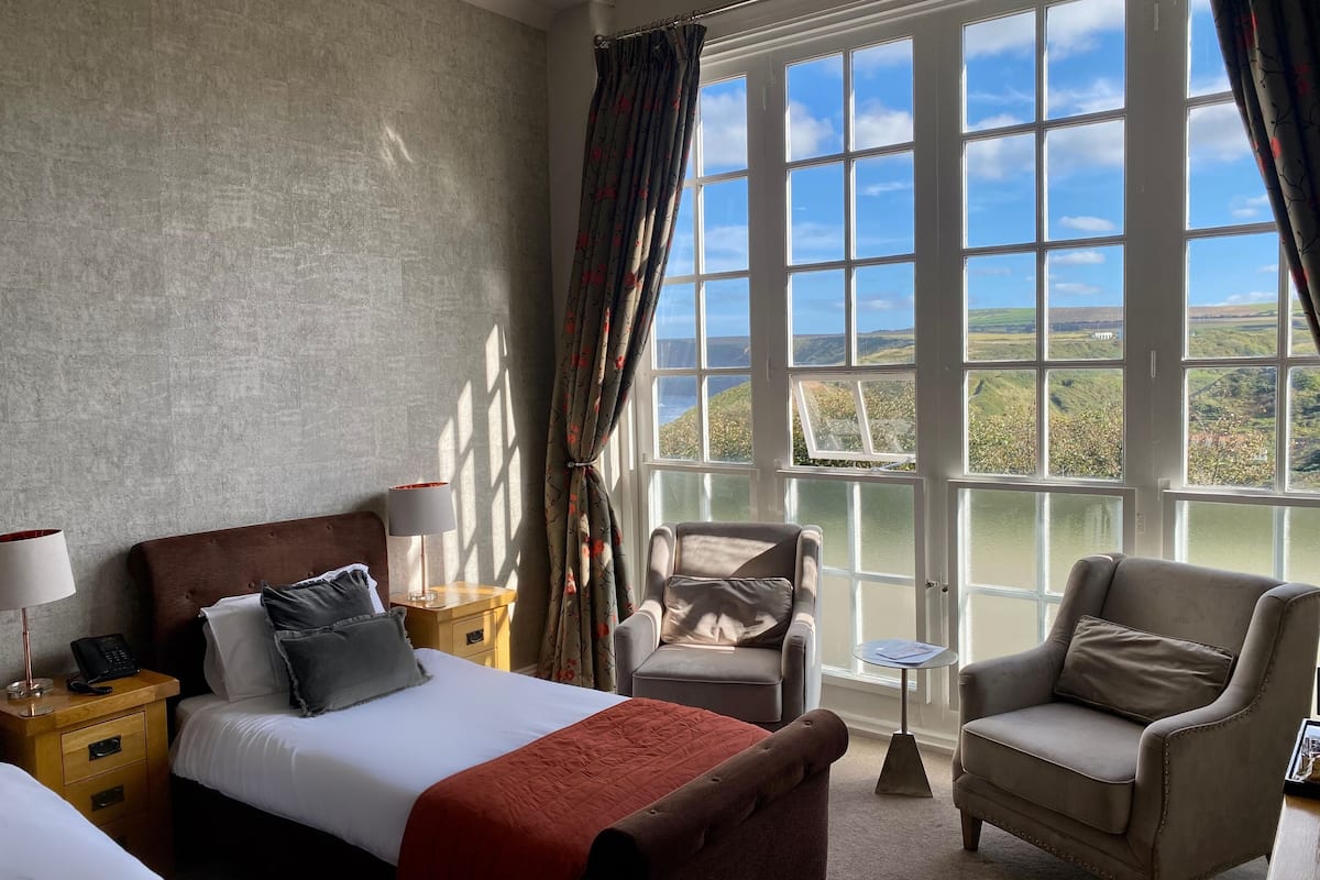 A hotel room with a bed, a chair, a small table, and a view of the countryside through large windows.