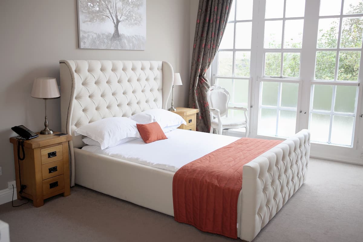 A bedroom with a large bed, a bedside table with a lamp, a chair, and a window with curtains.